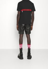Camiseta de algodón negra con una franja horizontal roja, combinada con pantalones cortos de cuero negros, calcetines a rayas rojas y blancas, y botas de plataforma negras.