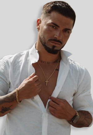 Weißes Leinenhemd mit offenem Kragen, goldene Halskette mit einem Kreuz, sichtbare Tattoos und einen strukturierten, hellen Hautton.
