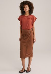 Top de culoare ruginită, cu un decolteu plisat, asortat cu o fustă închidera brown, cu nasturi pe lateral. Purtați cu sandale maronii cu curele.