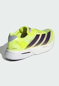 Scarpa atletica di un brillante giallo con tomaia in rete, strisce decorative viola e suola bianca. Presenta un retro testurizzato e un design leggero.