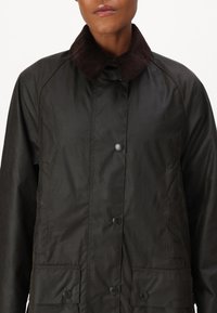 Black, water-resistant jacket with a corduroy collar, snap buttons, and two front pockets. Features a relaxed fit and smooth texture.
