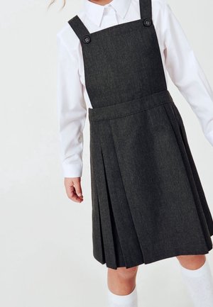 Robe salopette gris foncé avec des bretelles ajustables et des accents de bouton, dotée de plis à la jupe. Chemise blanche à manches longues en dessous.