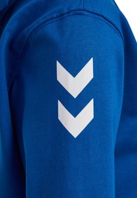 Blauwe trui met een gladde textuur en drie witte chevronstrepen op de linker mouw. Ontworpen voor casual gebruik.