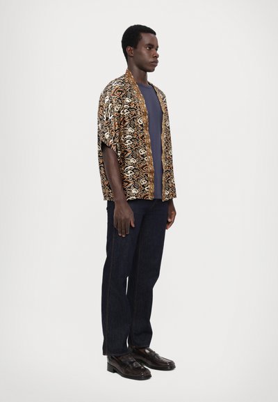 Krátký rukáv, otevřený kimono v černé barvě se zlatými a hnědými vířícími vzory, nošené přes námořnické tričko, v kombinaci s tmavými džíny a botami.