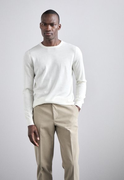 Helle beige langärmlige Pullover aus weichem, strukturiertem Stoff. Kombiniert mit hellbraunen Hosen. Einfacher Rundhalsausschnitt, taillierte Passform.