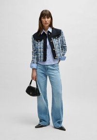 Tweedjacka i blått och svart med guldknappar, kombinerad med en ljusblå skjorta och vida denimjeans. Liten svart handväska och spetsskor.