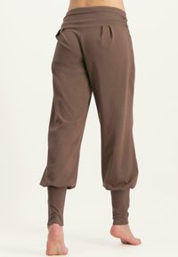Braune, weiche Stoffhosen mit einem breiten Bund, Falten am Rücken und taillierten Beinen. Sie sind locker geschnitten und haben Bündchen an den Knöcheln.