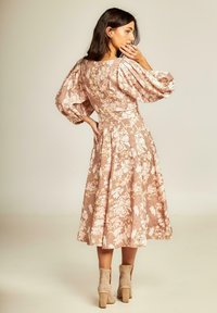 Bloemen midi-jurk in lichtroze met pofmouwen, gestructureerde stof en een getailleerde taille. Gecombineerd met beige enkelboots met uitsnijdingen.