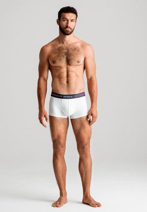 Weiße Boxershorts mit einem dunklen Bund, der rote Akzente aufweist. Modell steht barfuß da und präsentiert ein enganliegendes Design und eine glatte Textur.