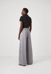 Polo noir à manches courtes associé à un pantalon large gris taille haute avec une bande satinée sur le côté et des fines rayures.