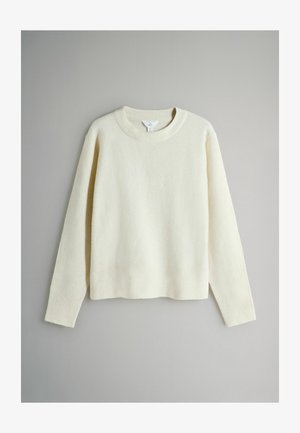 Krämfärgad tröja gjord av mjukt, texturerat tyg. Har rund halsringning, långa ärmar samt ribbade muddar och fåll.