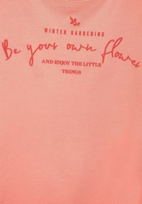 Koralfärgad T-shirt i mjukt tyg med texten "WINTER GARDENING Var din egen blomma OCH NJUT AV DE SMÅ SAKERNA" i kontrasterande röd.