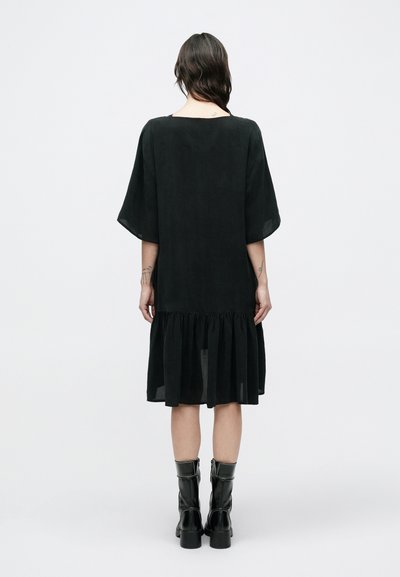 Μαύρο φόρεμα με χαλαρή εφαρμογή, κοντά, φαρδιά μανίκια και βολάν στο τελείωμα. Κατασκευασμένο από απαλό ύφασμα με λεία υφή.
