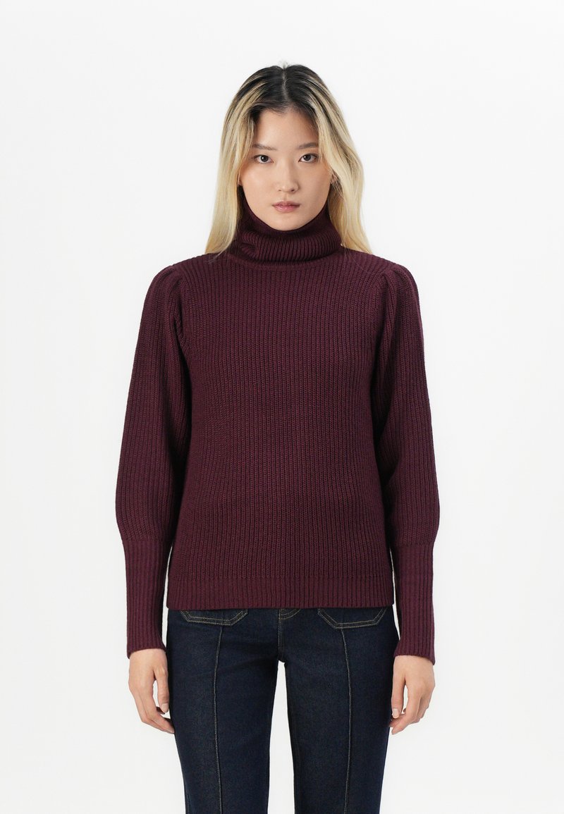 Burgundy polotröja med ribbad textur, åtsittande ärmar och avslappnad passform, tillsammans med mörkblå jeans.