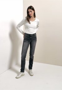 Musta korkeavyötäröinen farkut, yhdistettynä istuvaan valkoiseen pitkähihainen toppiin ja valkoisiin tennareihin. Sileä koostumus, klassinen muotoilu.