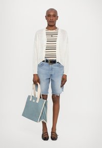 Hvit strikket cardigan, stripete beige og svart topp, lyseblå denimshorts, svart belte med sirkulært beslag, bærende en teal tote bag, svarte flate sko.
