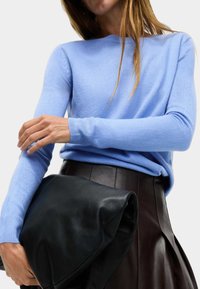 Ljusblå kashmirtröja med räfflade ärmar, tillsammans med en svart läderhandväska och en mörk plisserad kjol, som visar upp mjuka texturer.