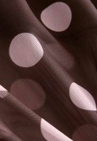 Tissu en maille marron avec de gros pois roses irréguliers. Texture transparente, légère, avec un motif à carreaux subtil dans le matériau.