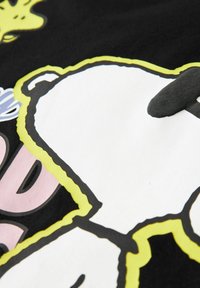 Musta kangas, jossa on valkoisen ja keltaisen piirroskarhun kuvio, jossa on vaaleanpunaiset aksentit. Kuvio on voimakkaasti ääriviivattu ja pinnaltaan sileä.