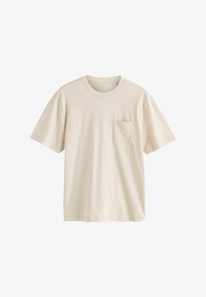 Világos bézs színű, rövid ujjú póló, pamutból készült. Kerek nyakkivágással és egy kis elülső zsebbel rendelkezik. Simaság jellemzi, laza szabású.