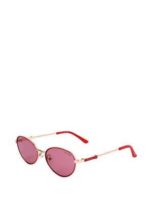 Occhiali da sole rotondi con lenti rosa, sottili montature dorate e aste rosse, con il logo Guess sui lati.