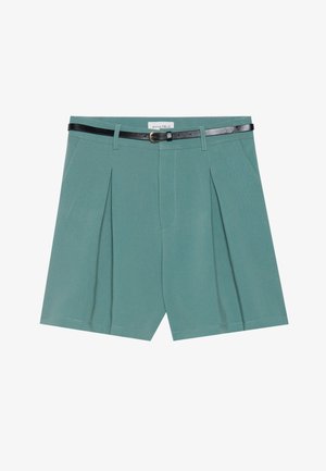 Bermudas verdes ajustadas com pregas frontais, design estruturado e um cinto preto fino com uma fivela circular. Textura de tecido suave.