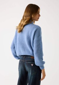 Maglione lavorato a maglia azzurro chiaro con un motivo testurizzato, caratterizzato da una vestibilità comoda e spalle scese. Indossato con jeans scuri, mostrando il dettaglio sul retro.