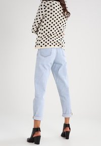 Suéter beige con lunares negros, jeans de tiro alto azul claro, puños enrollados y zapatos de tacón abiertos negros.