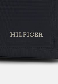 Borsa in materiale texture blu navy con il logo argento "HILFIGER" al centro, dalla forma rettangolare elegante e con dettagli di cucitura sottili.