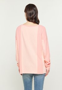 Maglietta a maniche lunghe in rosa chiaro, con un design a blocchi di colore in diverse sfumature. Tessuto morbido, vestibilità ampia e spalle scese.