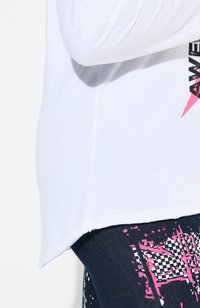 Chemise blanche à manches longues avec un ourlet qui descend sur les côtés. Présente un design graphique rose et noir. Assortie à des leggings bleus ornés d'un motif.