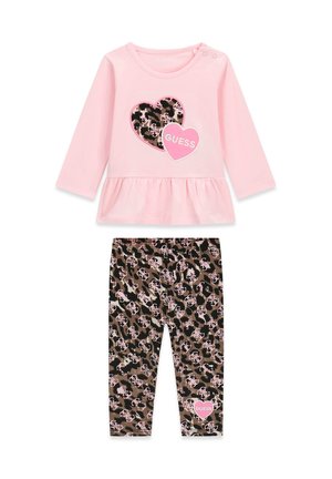 Pinkes Langarmoberteil mit zwei Herzmotiven, kombiniert mit braunen und schwarzen Leopardenmusterhosen, die ein kleines pinkes Herz mit dem Text "GUESS" zeigen.