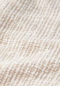 Strukturierter Stoff in sanftem Weiß mit subtilen cremefarbenen Sprenkeln, der ein gestricktes Muster und eine plüschige, leicht flauschige Oberfläche aufweist.