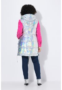 Holografische puffer vest met een capuchon, voorzien van een glanzend, reflecterend oppervlak en trekkoorddetails, gedragen over een roze trui met sterpatroon.