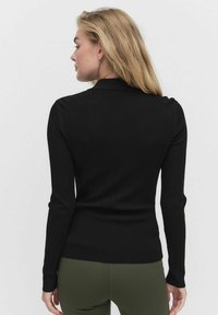 Svart ribbad långärmad topp med en åtsittande design, som har en liten krage och mjuk textur. Bärs med olivgröna byxor.