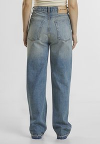 Široke denim hlače v svetlo modrem odtenku. Lastnosti vključujejo visok pas, dva zadnja žepa in strgane robove. Oznaka blagovne znamke na hrbtni strani pasu.