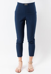 Pantaloni alla caviglia blu navy su misura in tessuto liscio, con una fibbia frontale in tonalità oro e pieghe frontali ben definite.