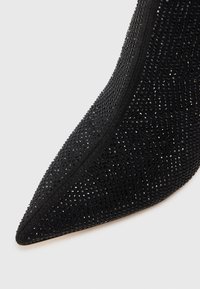 Talons aiguilles noirs avec un bout pointu, recouverts d'un tissu texturé avec de petits strass noirs formant un motif scintillant.