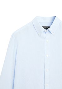 Chemise bleu clair à manches longues avec boutons, col boutonné et boutons blancs, étiquette de la marque visible à l'intérieur du col.
