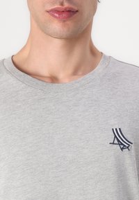 Tricou din bumbac gri, cu decolteu rotund și un mic design brodat în bleu marin pe partea stângă a pieptului. Textură moale și stil minimalist.