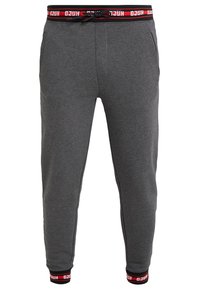 Graue Jogginghose aus weichem Stoff, mit einem Kordelzugbund, seitlichen Taschen und roten sowie schwarzen markierten Bündchen.