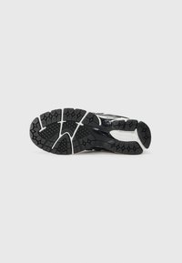Semelle de chaussure de sport noire avec une surface en caoutchouc texturé et différents motifs de semelle. Des accents blancs et un logo sont visibles.