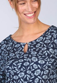 Dunkelbluse mit floralem Muster, Rundhalsausschnitt mit Schlitz, kurzen Ärmeln und gedruckten weißen Blumen mit grünen Blättern.