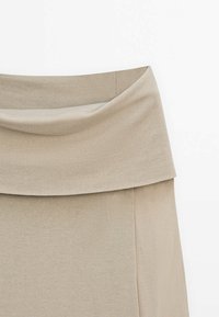 Beżowa spódnica z drapowanym pasem, wykonana z miękkiego materiału. Projekt cechuje gładka tekstura i prosty krój.