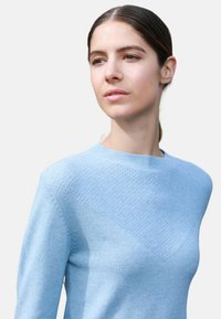 Pull en bleu clair présentant un motif texturé sur le devant supérieur, un col rond et des manches longues en tissu doux.