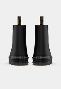 Botas de tobillo negras con un acabado suave, punta redonda y suela texturizada elevada. Presentan costuras doradas y lengüetas en la parte trasera para facilitar su uso.
