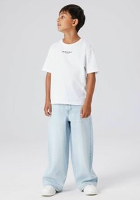 Balta īsroku T-krekls ar uzrakstu "Studio edition", kopā ar gaiši zilām plaša piegriezuma džinsa biksēm un baltām sporta apaviem. Ikdienišķs piegrieziens un relaksēts stils.