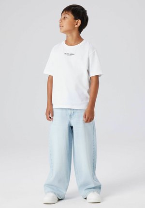 Bela majica s kratkimi rokavi s tekstom "Studio edition", kombinirana s svetlo modrimi širokimi jeans hlačami in belimi supergami. Prijeten kroj in sproščen slog.