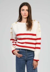 Pull en mélange de laine avec des rayures rouges sur fond crème, décolleté bateau, manches côtelées et boutons dorés décoratifs sur les épaules.