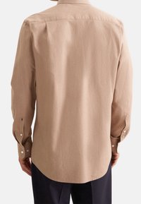 Camicia a maniche lunghe in beige, caratterizzata da una trama liscia e un orlo curvo. Polsini con bottoni e ricamo di piccolo logo vicino al polso.